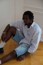 Person wearing a stripe shirt and denim shorts sitting on a wooden floor.